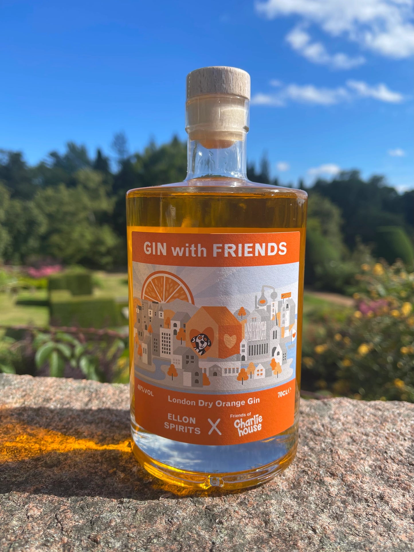 Premium “Gin with Friends” London Dry Orange Gin by Ellon Spirits and Friends of Charlie House — handcrafted citrus-infused gin bottle photographed outdoors in natural sunlight with a scenic garden background.