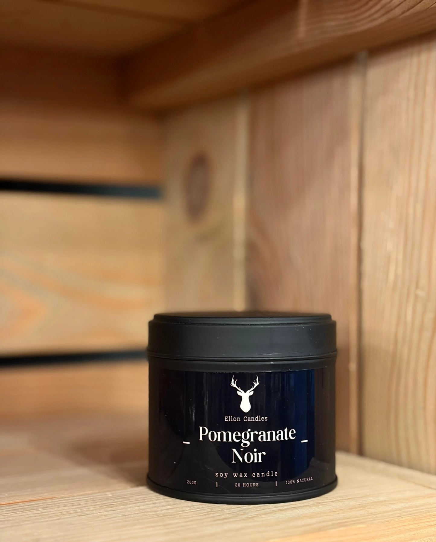 Candle jar labeled 'Pomegranate Noir' on a wooden shelf
