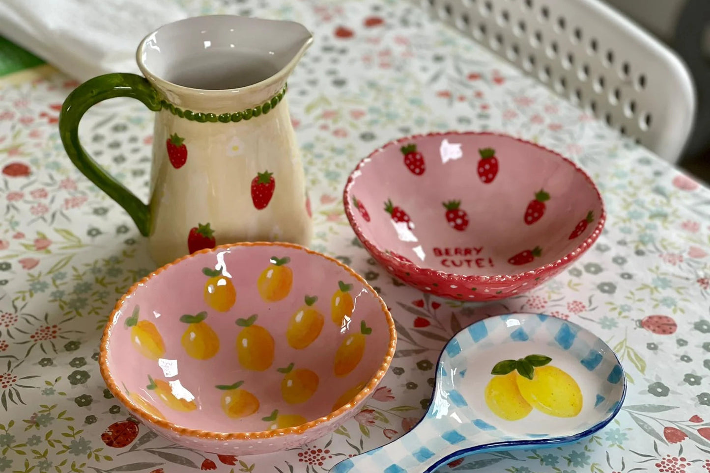 Set of ceramic dishes with strawberry and lemon designs on a floral tablecloth.