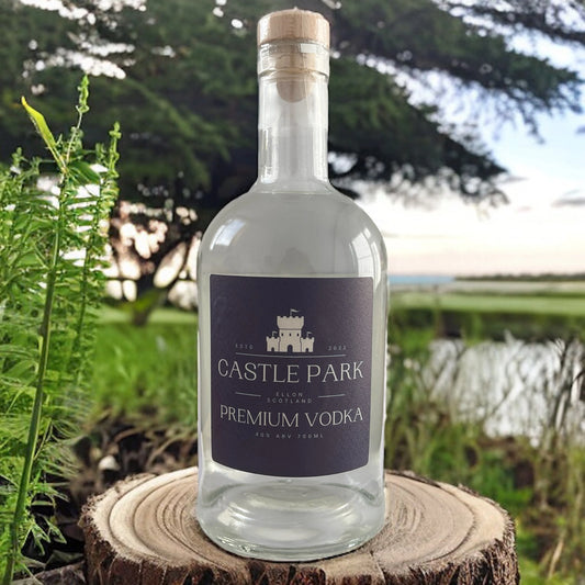 Castle Park Vodka bottle displayed outdoors on a tree stump with green foliage and countryside background – premium Scottish vodka from Ellon, Scotland.