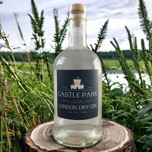 Castle Park London Dry Gin bottle displayed outdoors on a tree stump with green foliage and countryside background – premium Scottish gin from Ellon, Scotland.