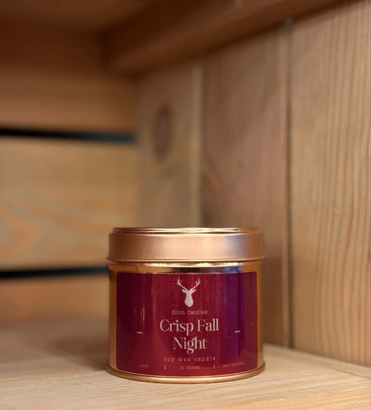 Candle in a tin labeled 'Crisp Fall Night' on a wooden surface