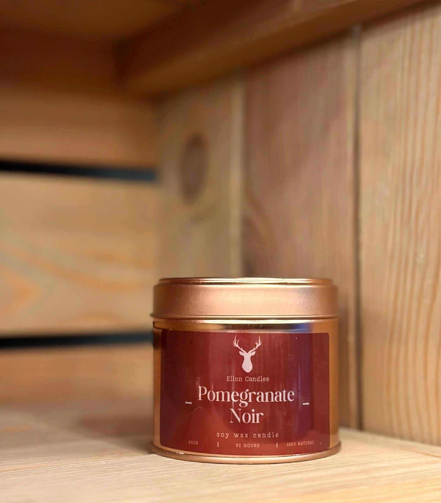 Candle in a red tin labeled 'Pomegranate Noir' on a wooden surface.