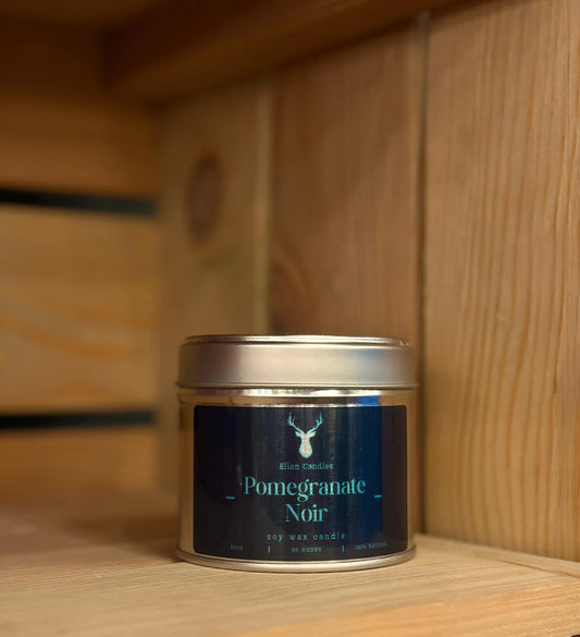 Candle tin labeled 'Pomegranate Noir' on a wooden shelf